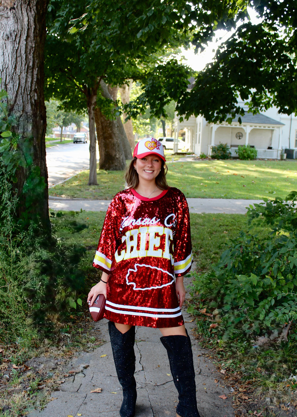 Person wearing a red sequin dress with 'Chiefs' text and a matching cap outdoors.