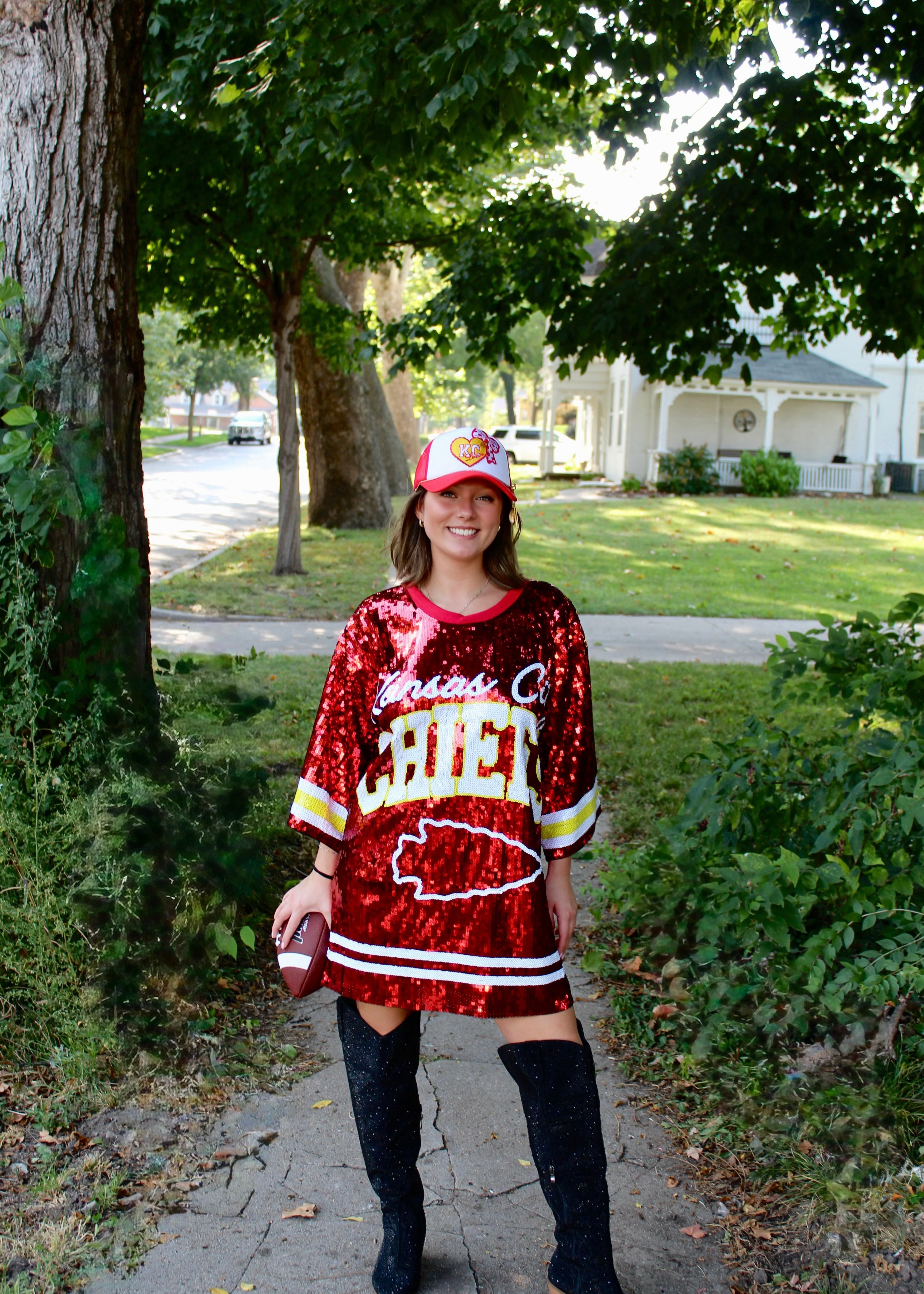 Person wearing a red sequin dress with 'Chiefs' text and a matching cap outdoors.